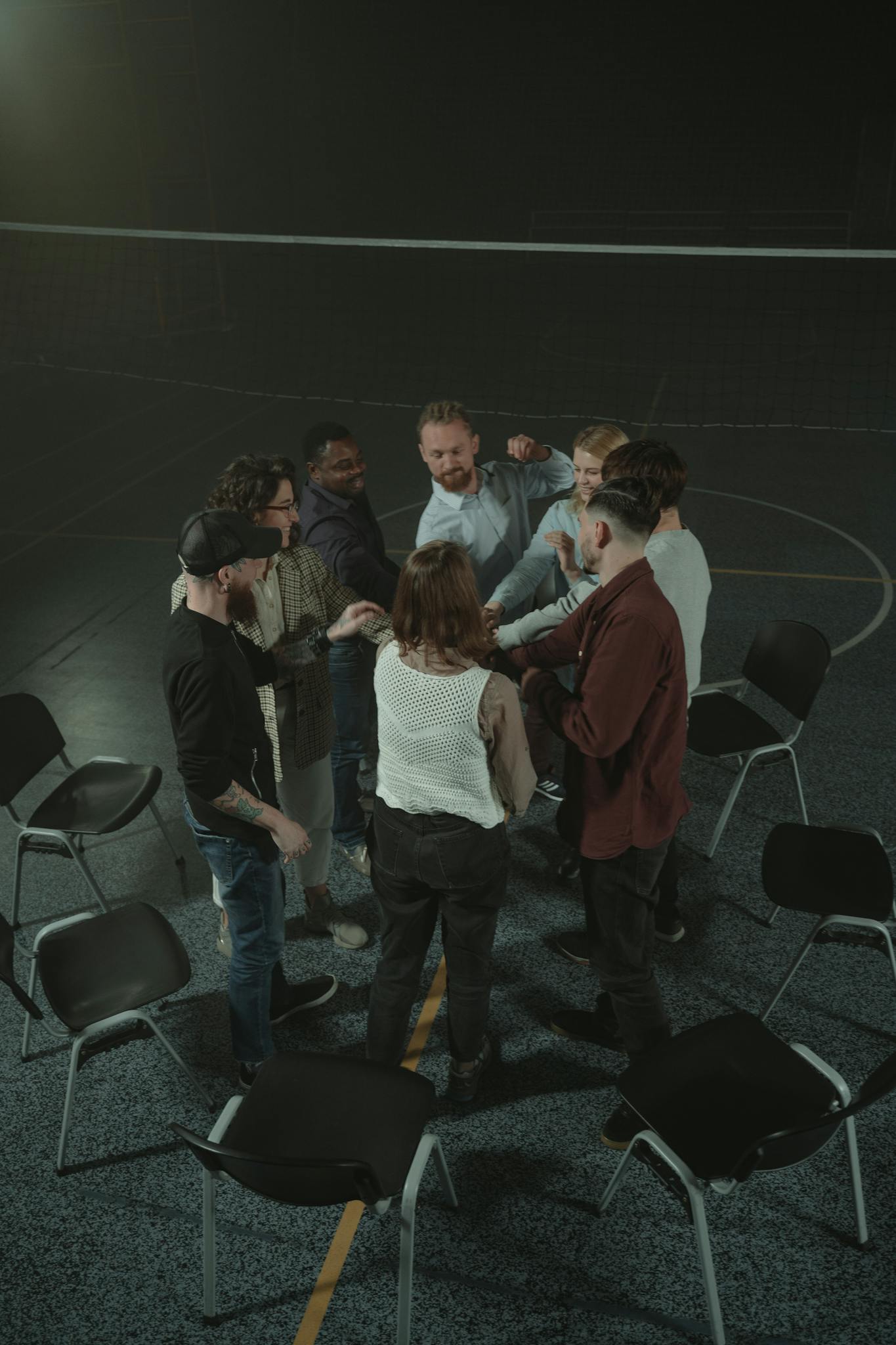 A group of adults engaged in a team-building activity indoors with chairs arranged in a circle.