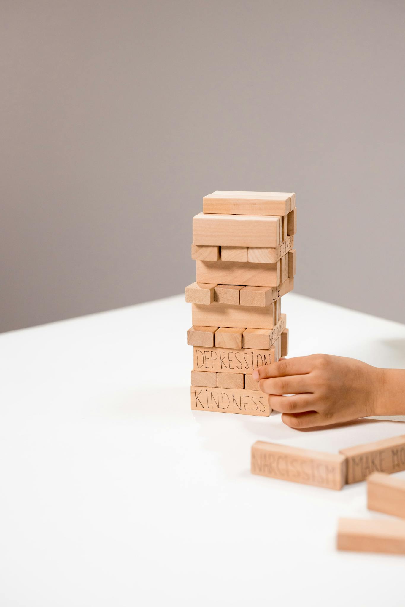 A hand stacks wooden Jenga blocks with words like depression and kindness.