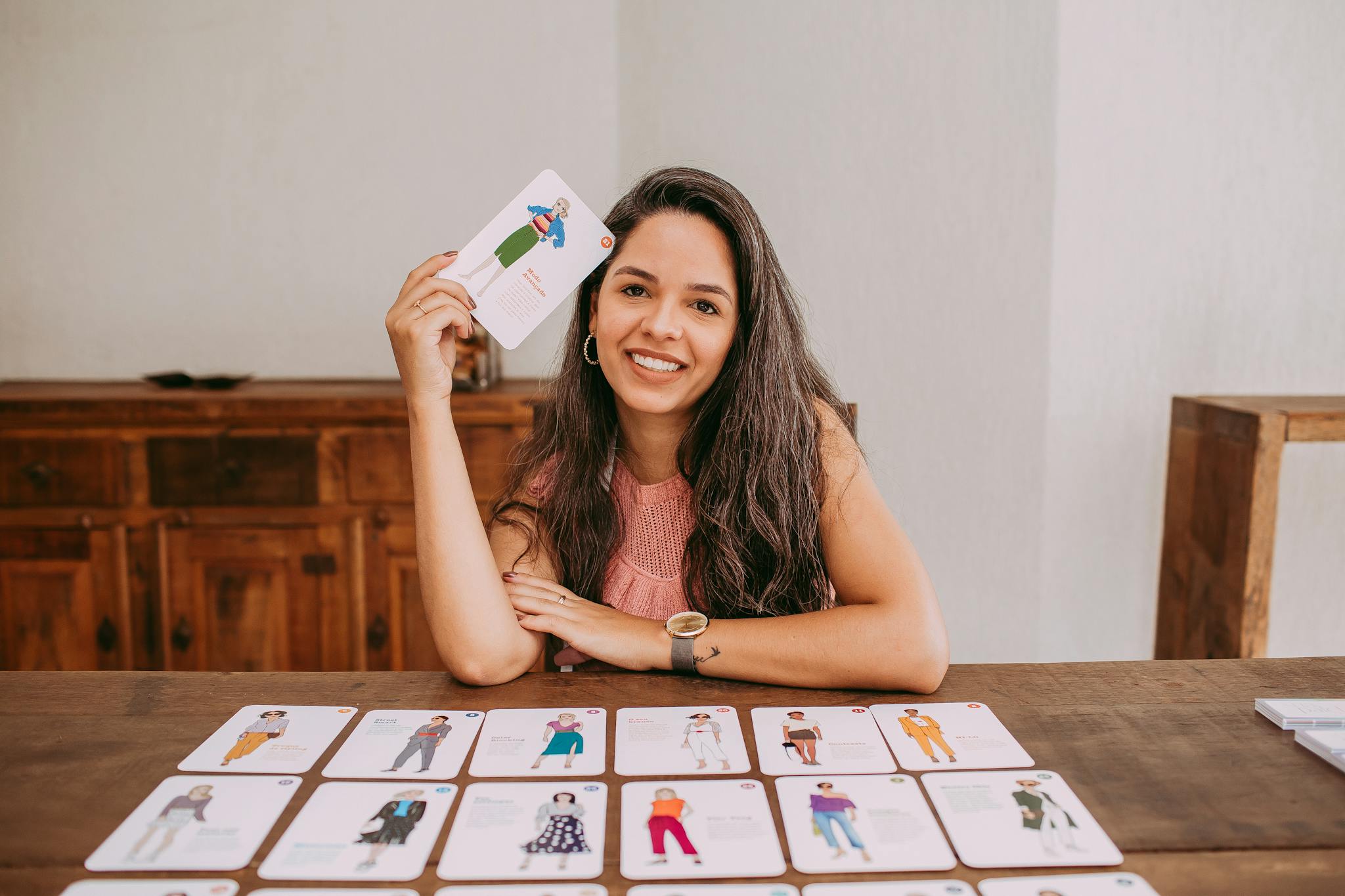 Woman with long hair holding educational cards, smiling at table, suitable for teaching context.